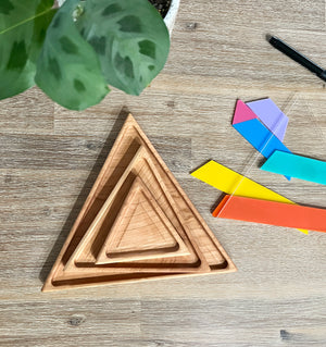 Nesting Triangle Pyramid Wooden Sensory Trays made of natural wood arranged on a wooden surface beside colorful geometric shapes, handcrafted homeschool education resources.