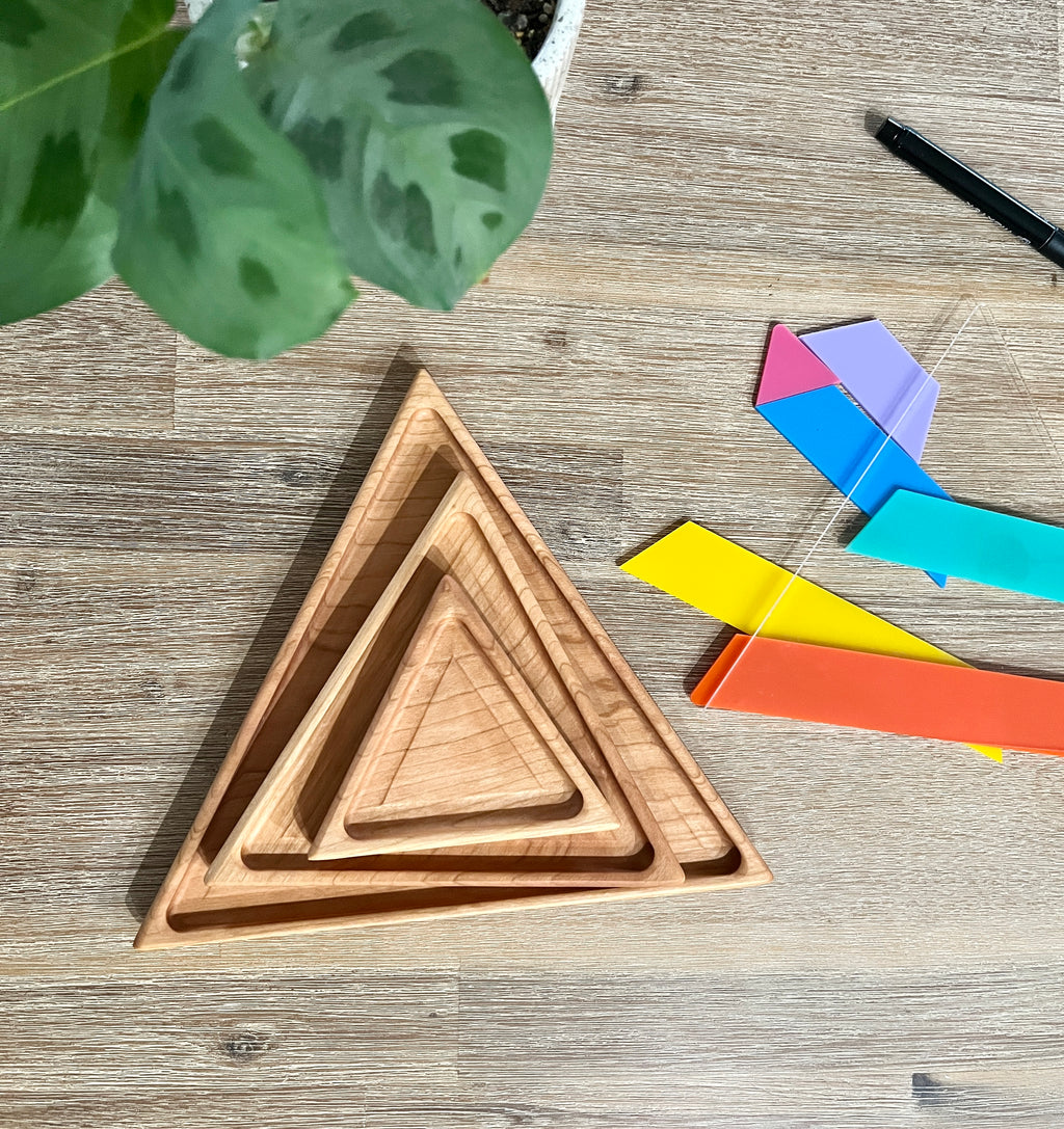 Nesting Triangle Pyramid Wooden Sensory Trays made of natural wood arranged on a wooden surface beside colorful geometric shapes, handcrafted homeschool education resources.