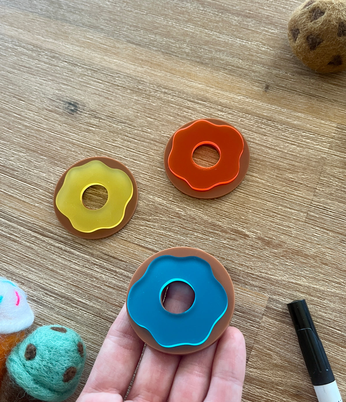 Little Dry Erasables - Donuts with Icing featuring three handcrafted wooden donut shapes with colorful translucent icing inserts, displayed with felt sensory balls and a black marker on a wood surface.