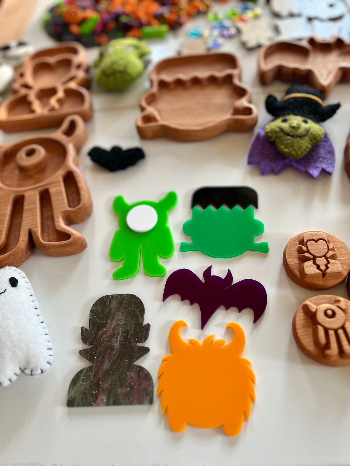 Assorted wooden and colorful acrylic Halloween-themed shapes and trays including monsters, bat, and ghost on white surface