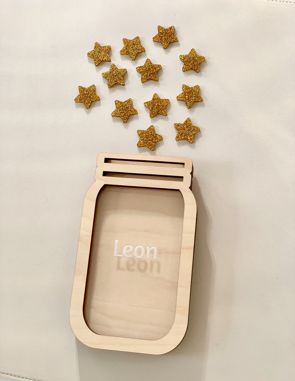 Wooden jar-shaped frame with the name Leon and scattered glittery gold star tokens on a light background