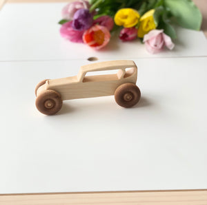 Light wooden toy car with large round wheels on a white surface with colorful flowers in the background