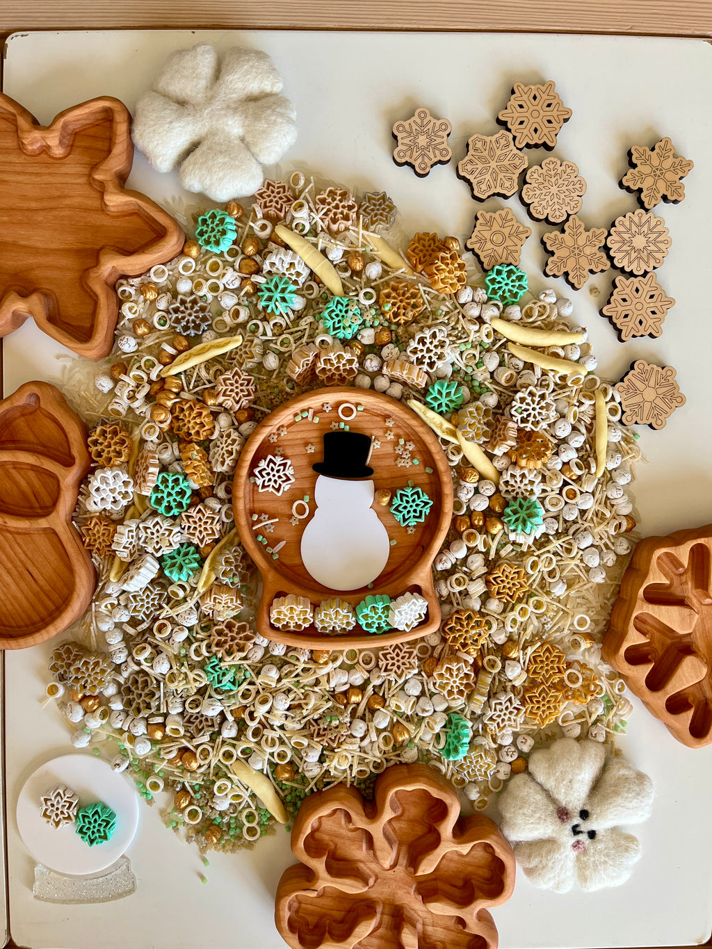 Wooden snowflake-shaped tray with felt flowers and scattered winter-themed beads and wooden snowflake pieces on table