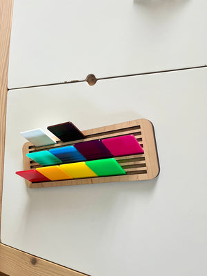 Wooden slotted base holding colorful translucent rectangular acrylic tiles arranged in three rows on white surface