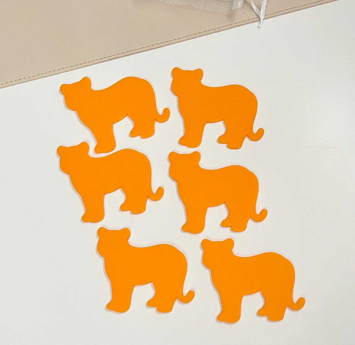Six bright orange cat-shaped pieces arranged on a white surface near a beige fabric edge