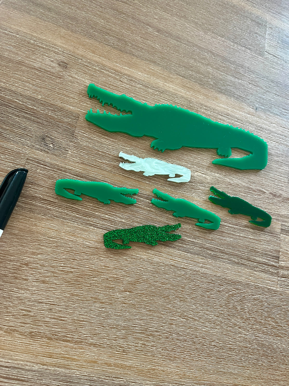 Little Dry Erasables - Crocodiles featuring handcrafted green and white crocodile shapes in various sizes made from wood and acrylic, displayed on a wooden surface with a black marker, homeschool educational resources.