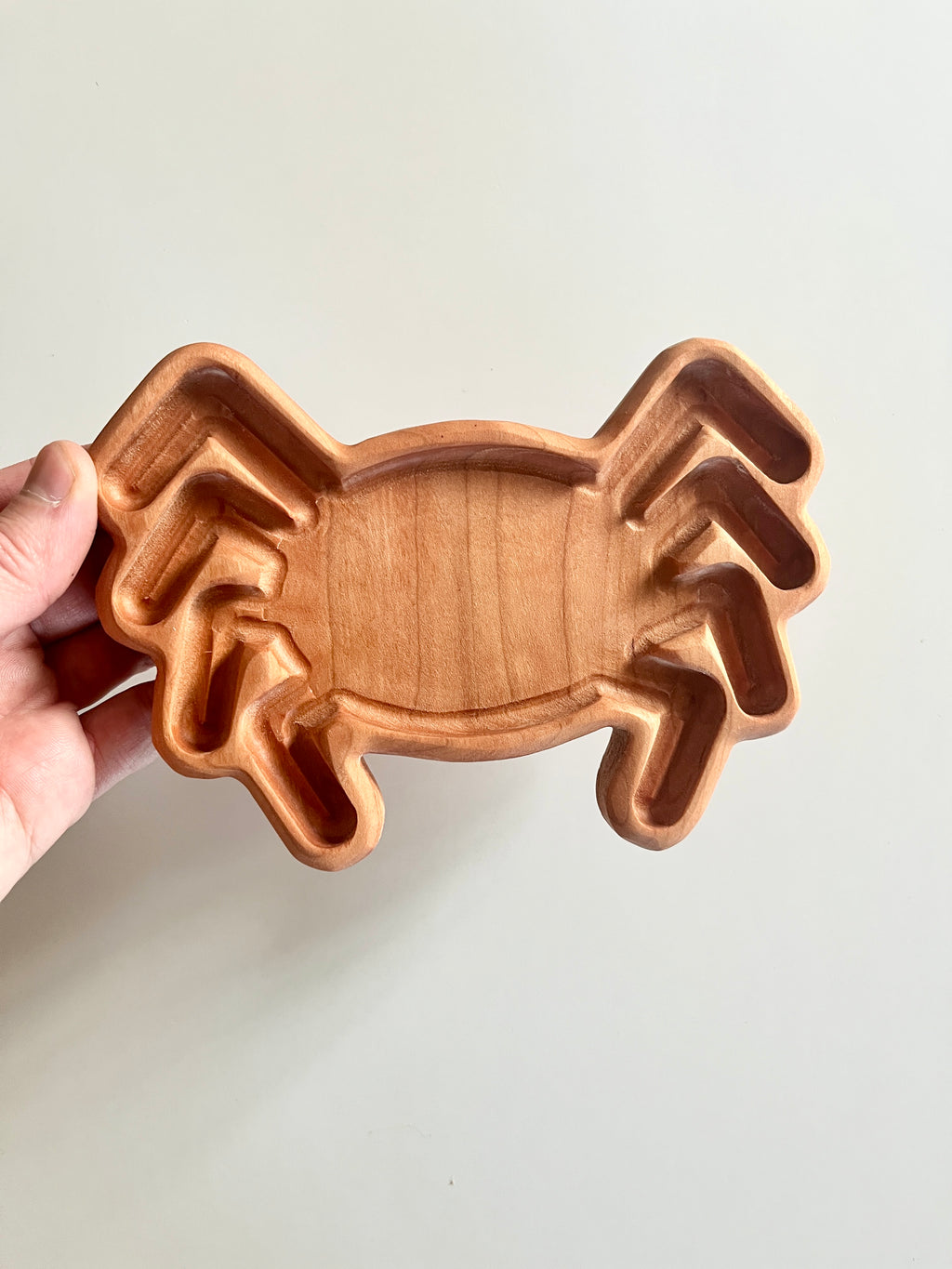 Hand-carved wooden tray shaped like a crab with smooth edges held against a plain light background