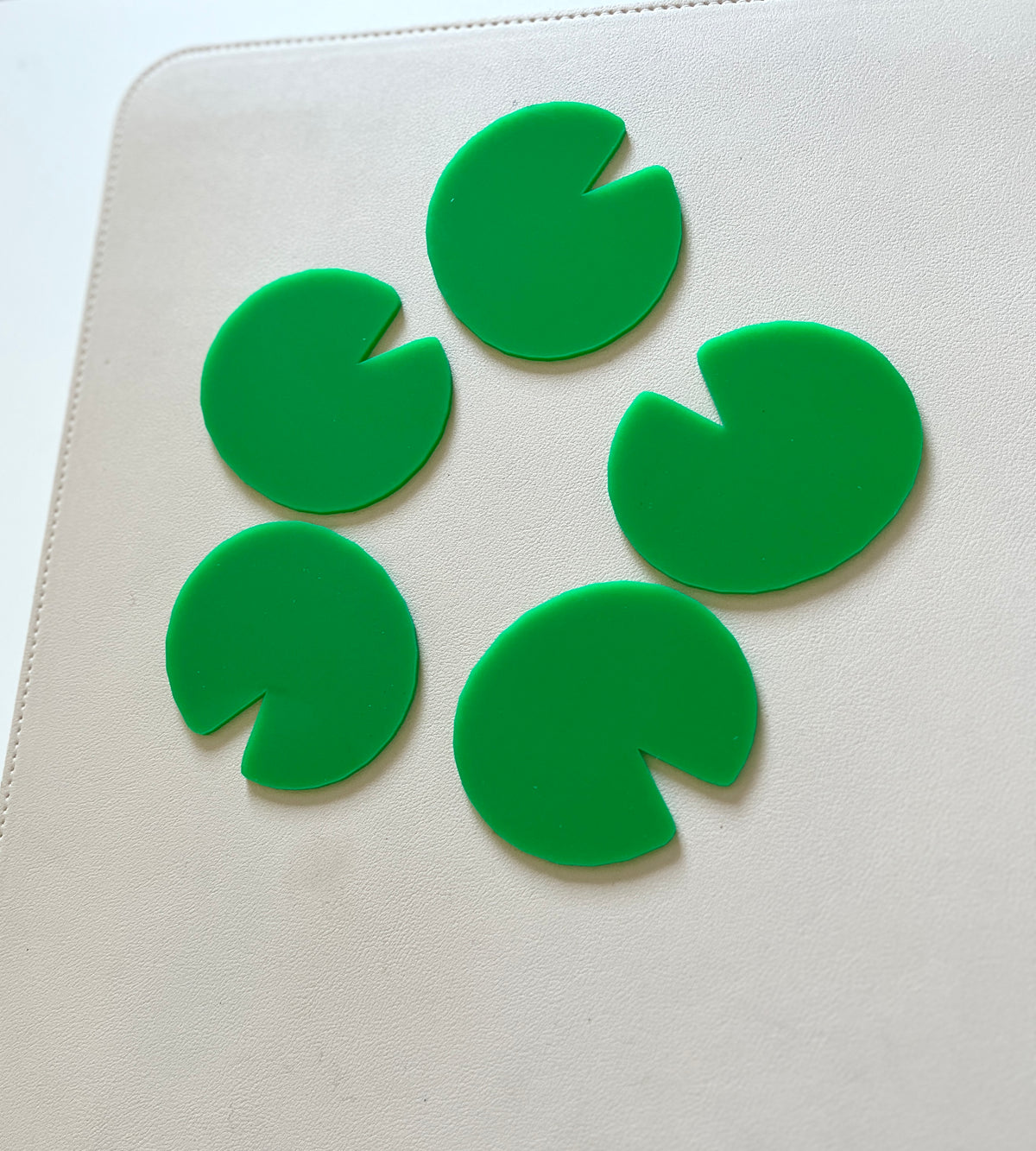 Five bright green plastic lily pad shapes arranged in a circle on a light beige surface