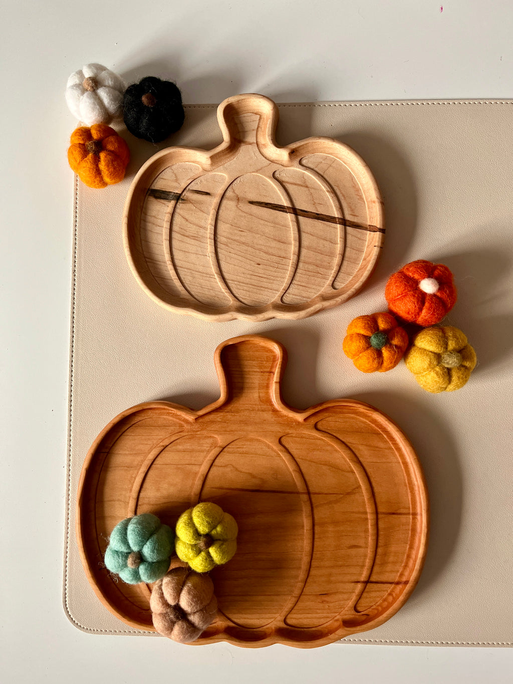 Two pumpkin-shaped wooden trays with small colorful felt pumpkins arranged around them on a light surface
