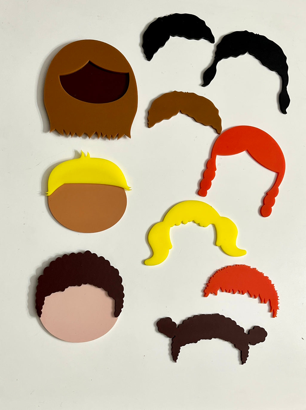 Colorful plastic face and hair shapes in various styles and skin tones arranged on a white background