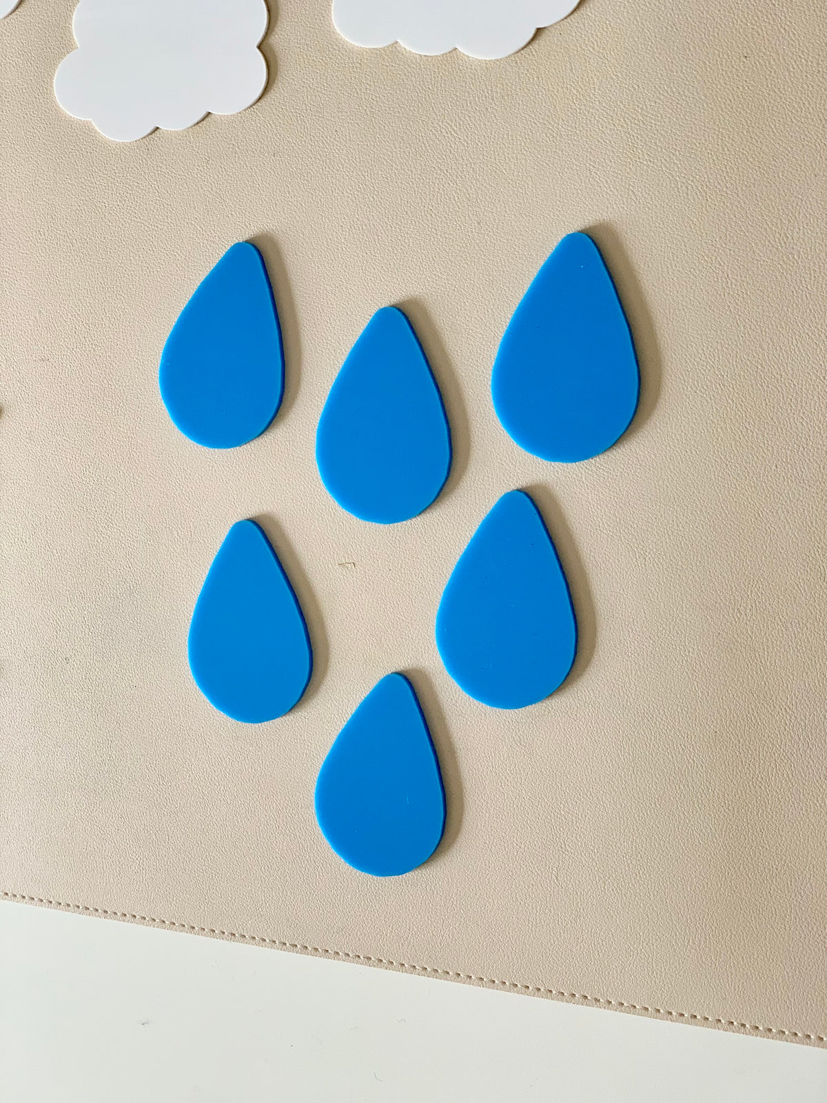 Six blue raindrop-shaped pieces arranged on a beige surface with two white cloud shapes above them