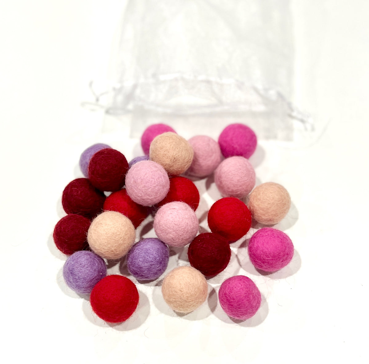 Cluster of small colorful felt balls in shades of red, pink, purple, and beige spilling out of a sheer white drawstring bag