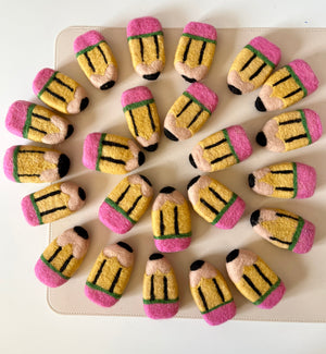 Twenty plush pencil-shaped toys with pink erasers and yellow bodies arranged in a circular pattern on a beige surface