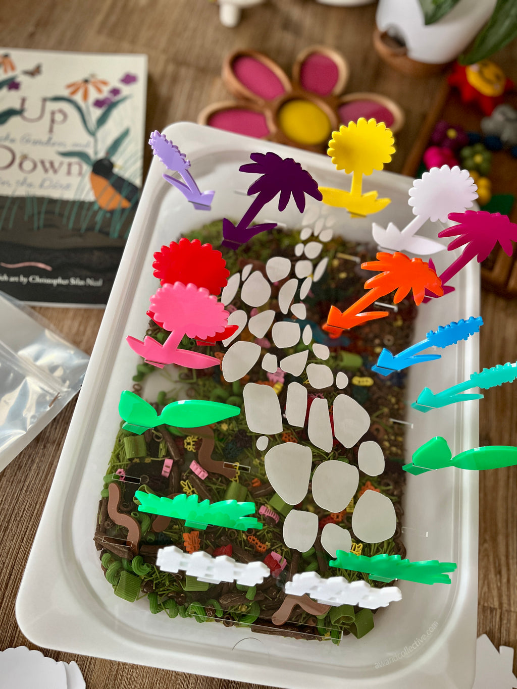 White tray with a nature-inspired base featuring colorful translucent acrylic pegs shaped like flowers and plants arranged along a stone path, showcasing STEM Insert – Acrylic Insert with Different Peg Options - Neighborhood, Veggie Garden, Flower Garden, Under the Sea + More, handcrafted, homeschool, education resources.