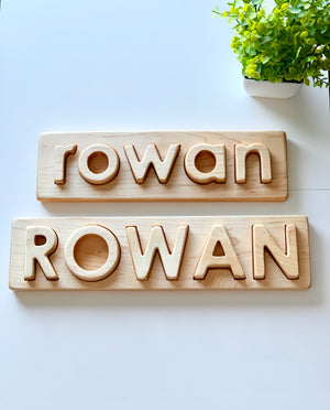 Personalized hardwood name puzzles with uppercase and lowercase letters spelling Rowan on wooden boards with plant nearby