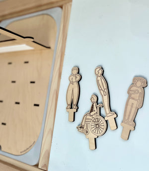 Laser-cut wooden figures depicting diverse characters including a person in a wheelchair on a light surface near a playboard