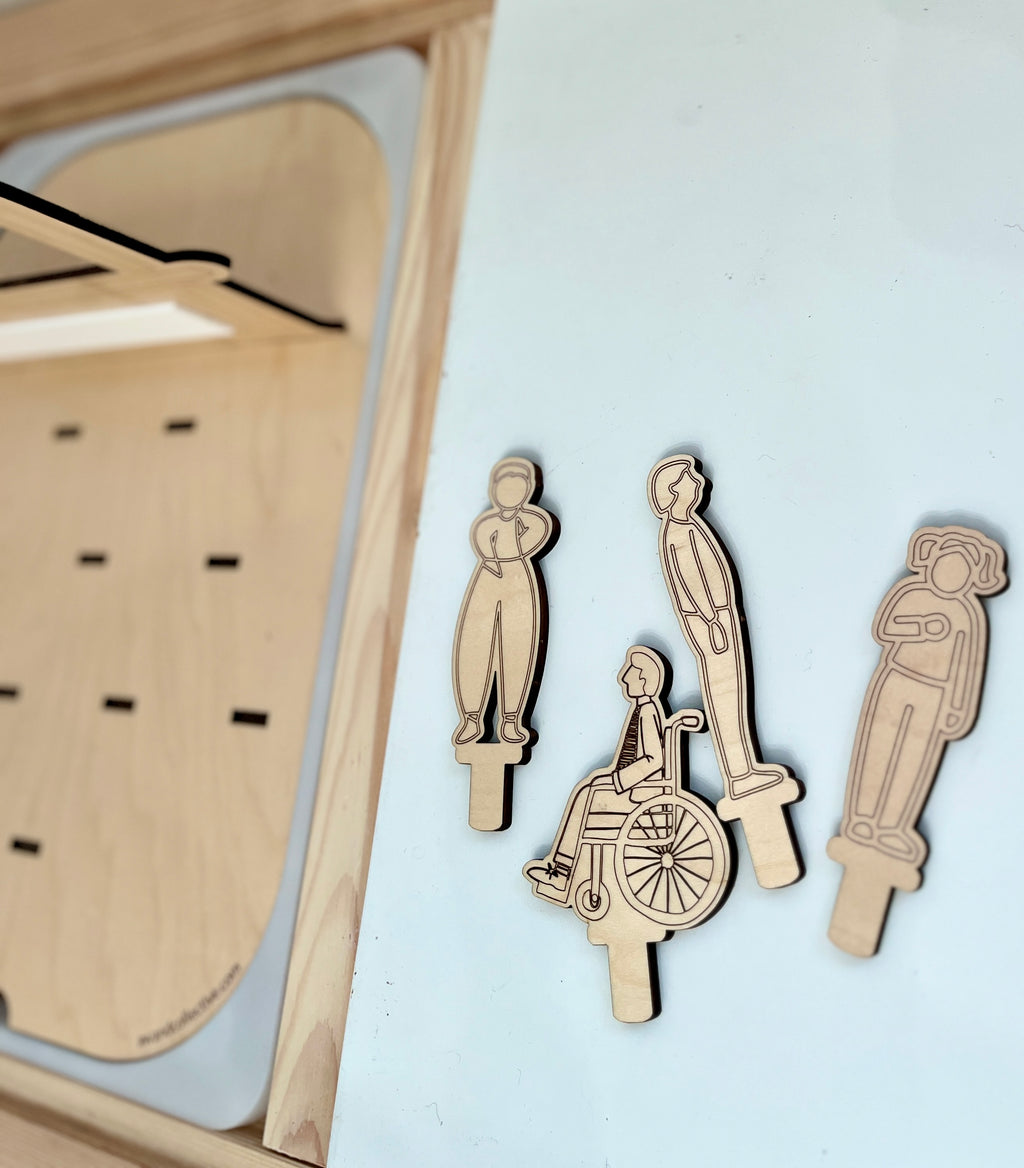 Laser-cut wooden figures depicting diverse characters including a person in a wheelchair on a light surface near a playboard