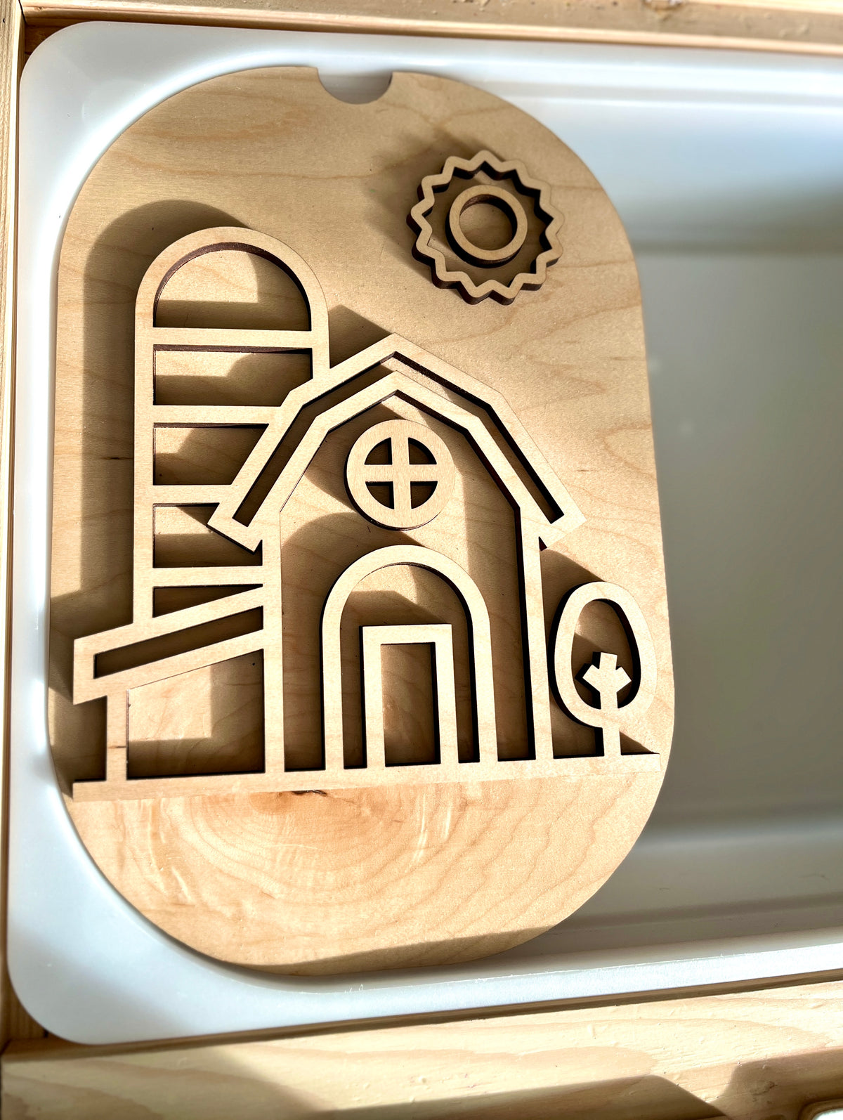 Light wooden puzzle board featuring a barn, silo, tree, and sun cutout shapes on a light surface