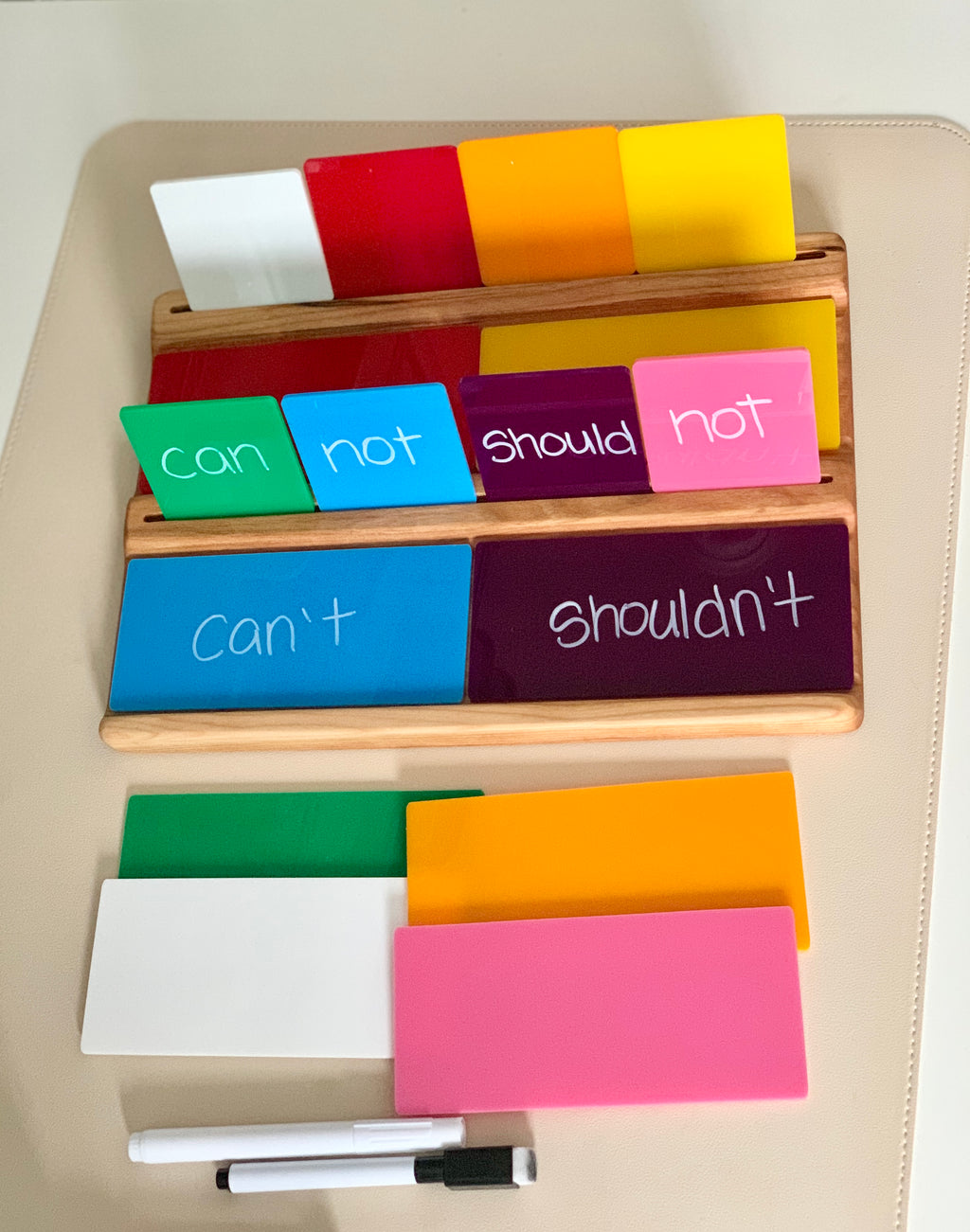 Wooden writing trays holding colorful language cards with words and contractions and two dry erase markers on beige surface