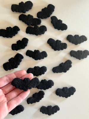 Multiple small black felt bat shapes scattered on a white surface with one held in hand