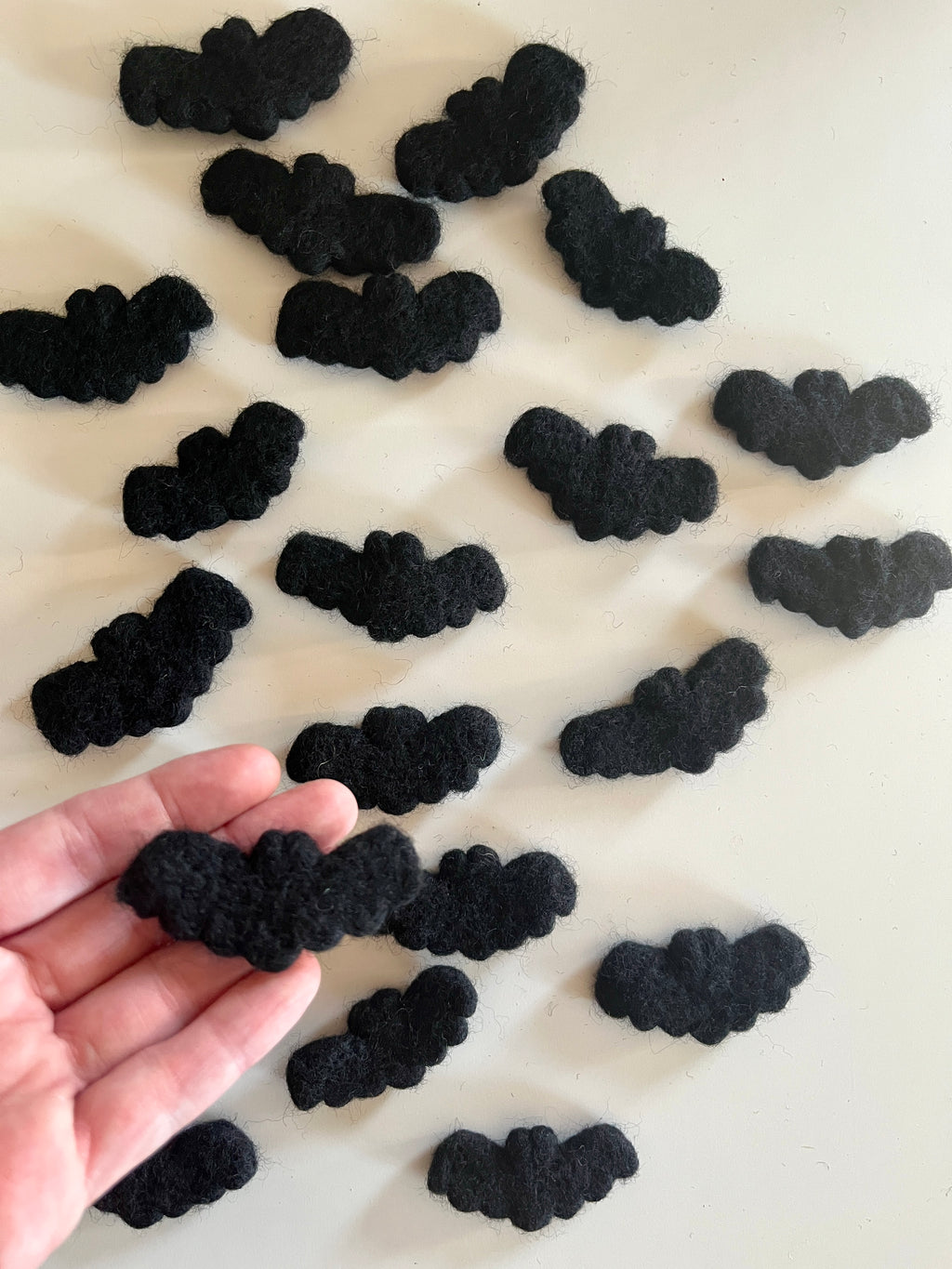 Multiple small black felt bat shapes scattered on a white surface with one held in hand