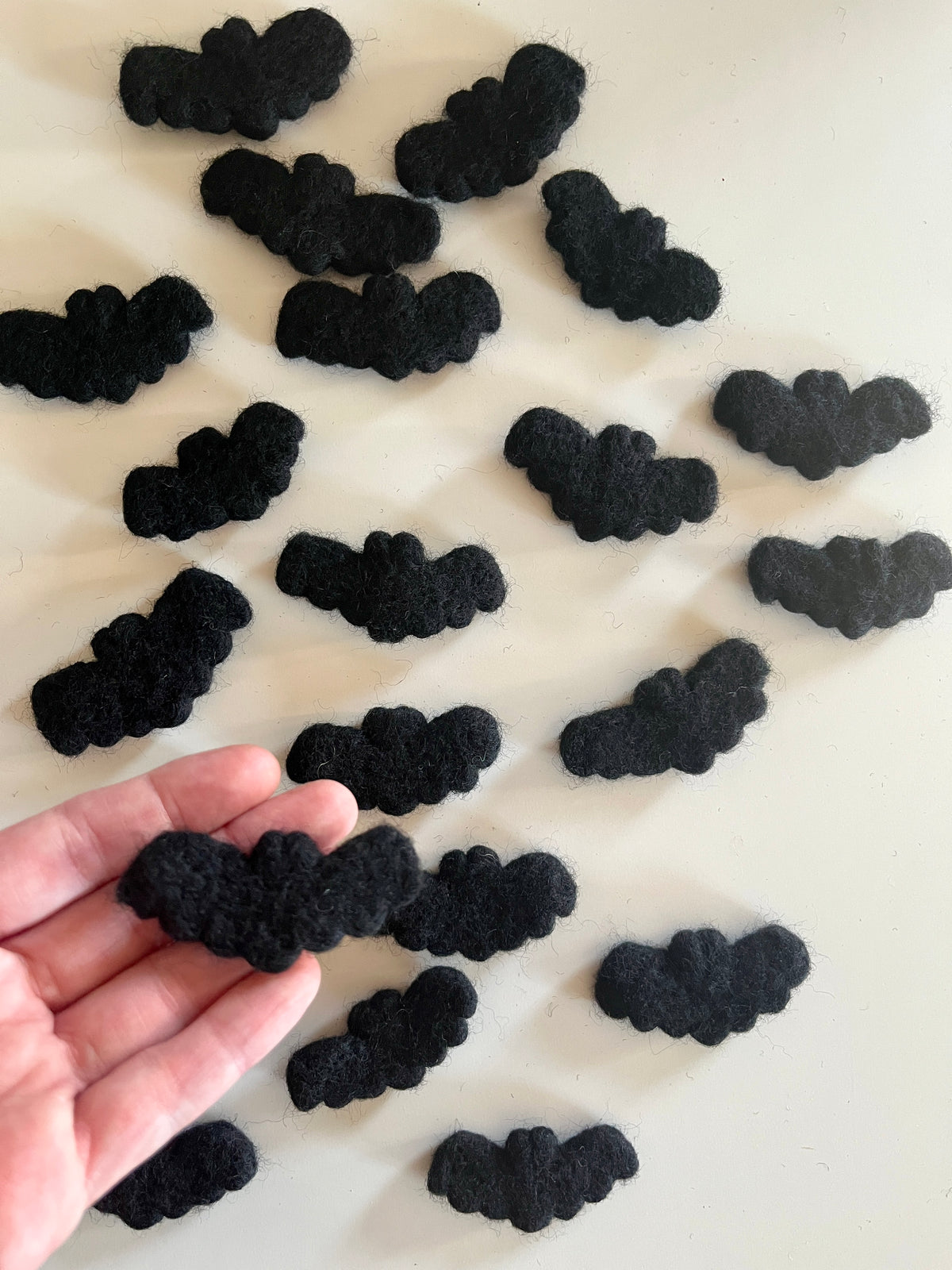 Multiple small black felt bat shapes scattered on a white surface with one held in hand