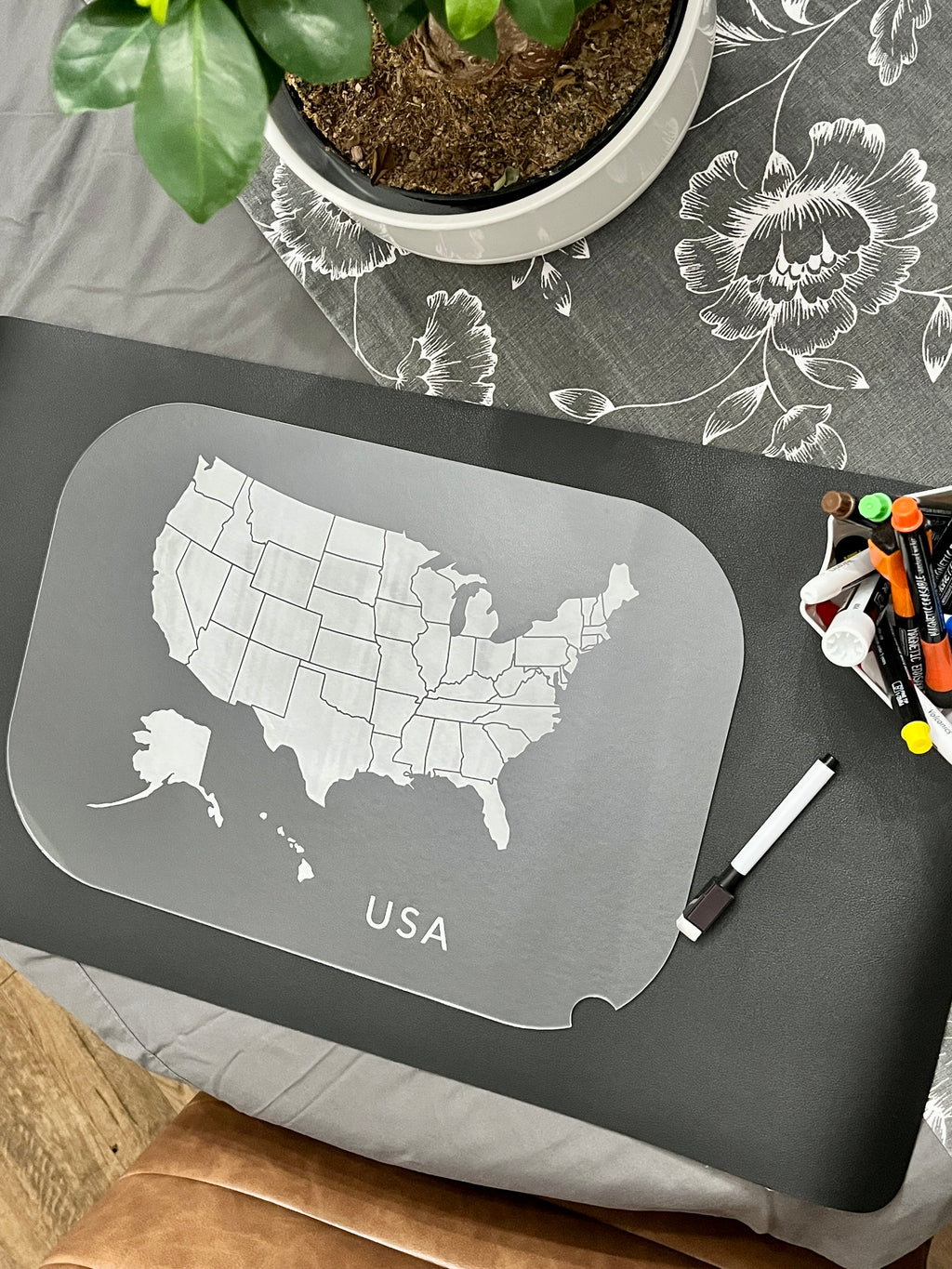 Gray placemat or writing board featuring an outlined map of the USA with state borders and a dry erase marker nearby
