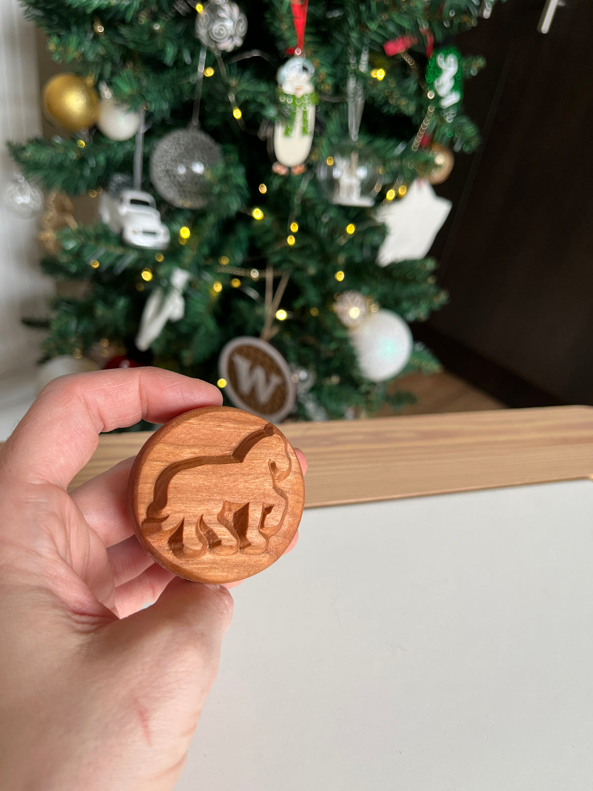Hand holding round wooden token with carved lion silhouette in front of decorated Christmas tree background