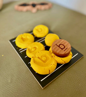 Wooden token with the letter "b" on yellow playdough balls arranged on a black and white striped card