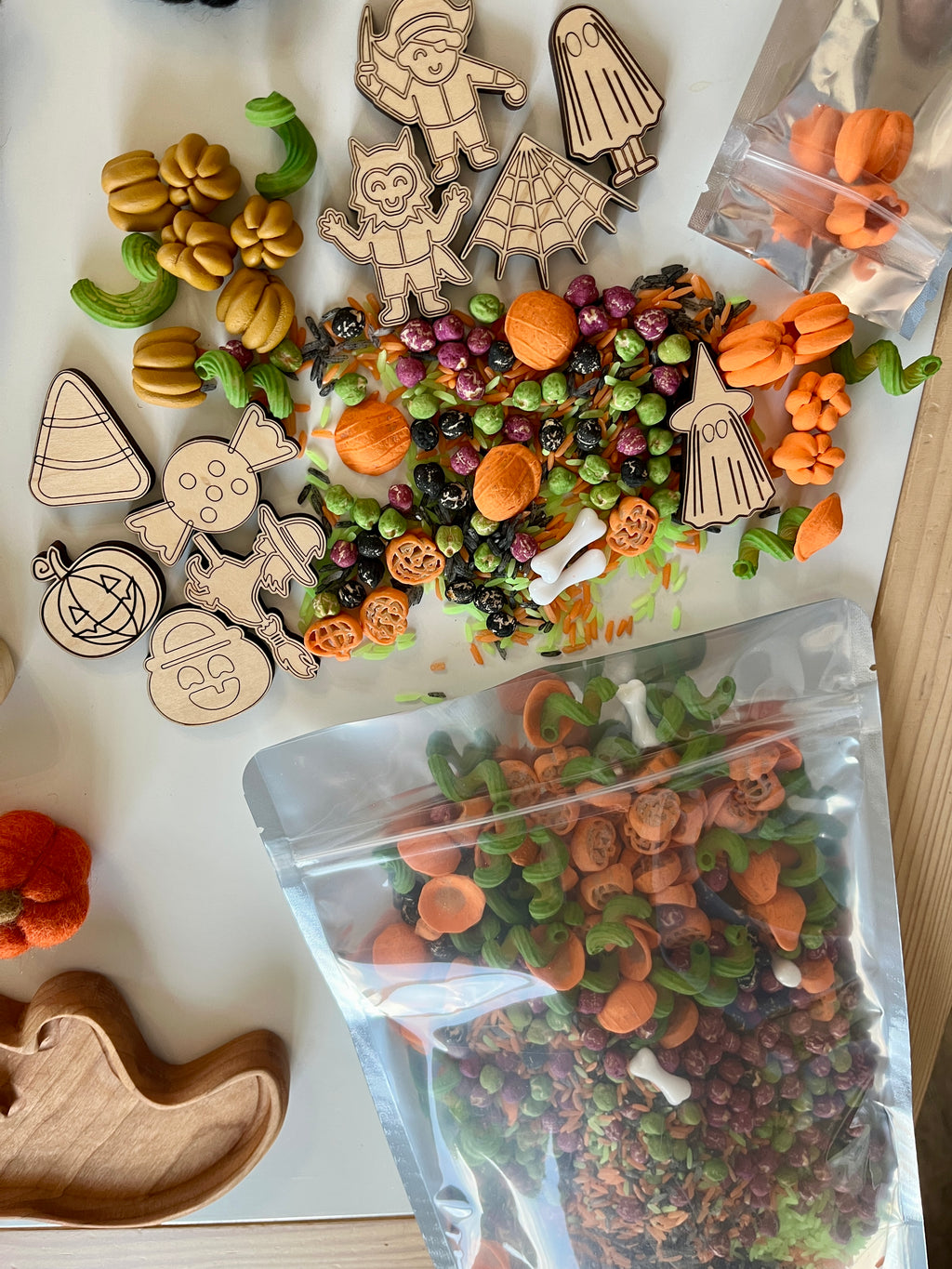 Halloween-themed sensory bin ingredients including wooden characters, colorful pasta, pumpkin shapes, and assorted small pumpkins on white surface