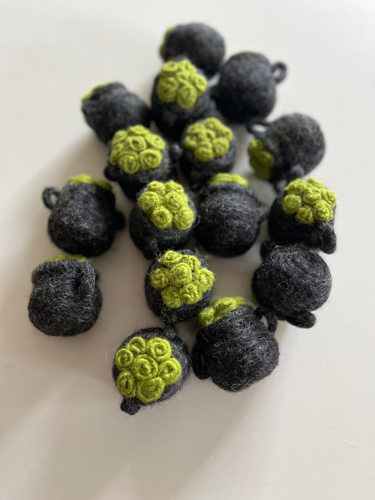 Small handmade black felt balls with green textured tops scattered on a white surface