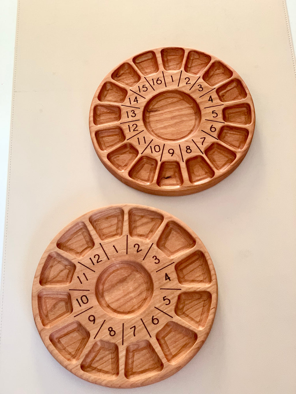 Two round wooden trays with numbered compartments arranged in circular patterns on a beige surface