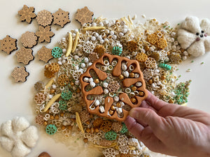 Hand holding wooden snowflake-shaped tray filled with mixed pasta and small winter-themed objects on white surface