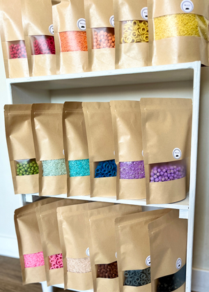 Assorted coloured sensory filler packs with rice, chickpeas, and pasta rings in kraft paper bags on white shelf