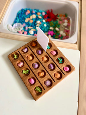 Wooden game board with rows of colorful seashell-shaped pieces and small green sea creature figures on a white table