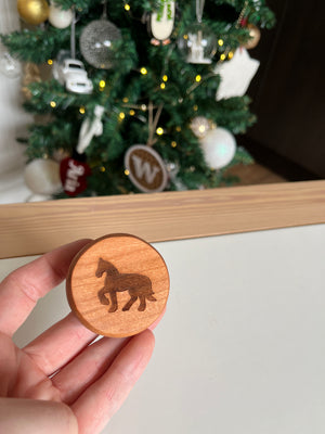 Hand holding round wooden token with engraved horse silhouette with decorated Christmas tree in soft focus background