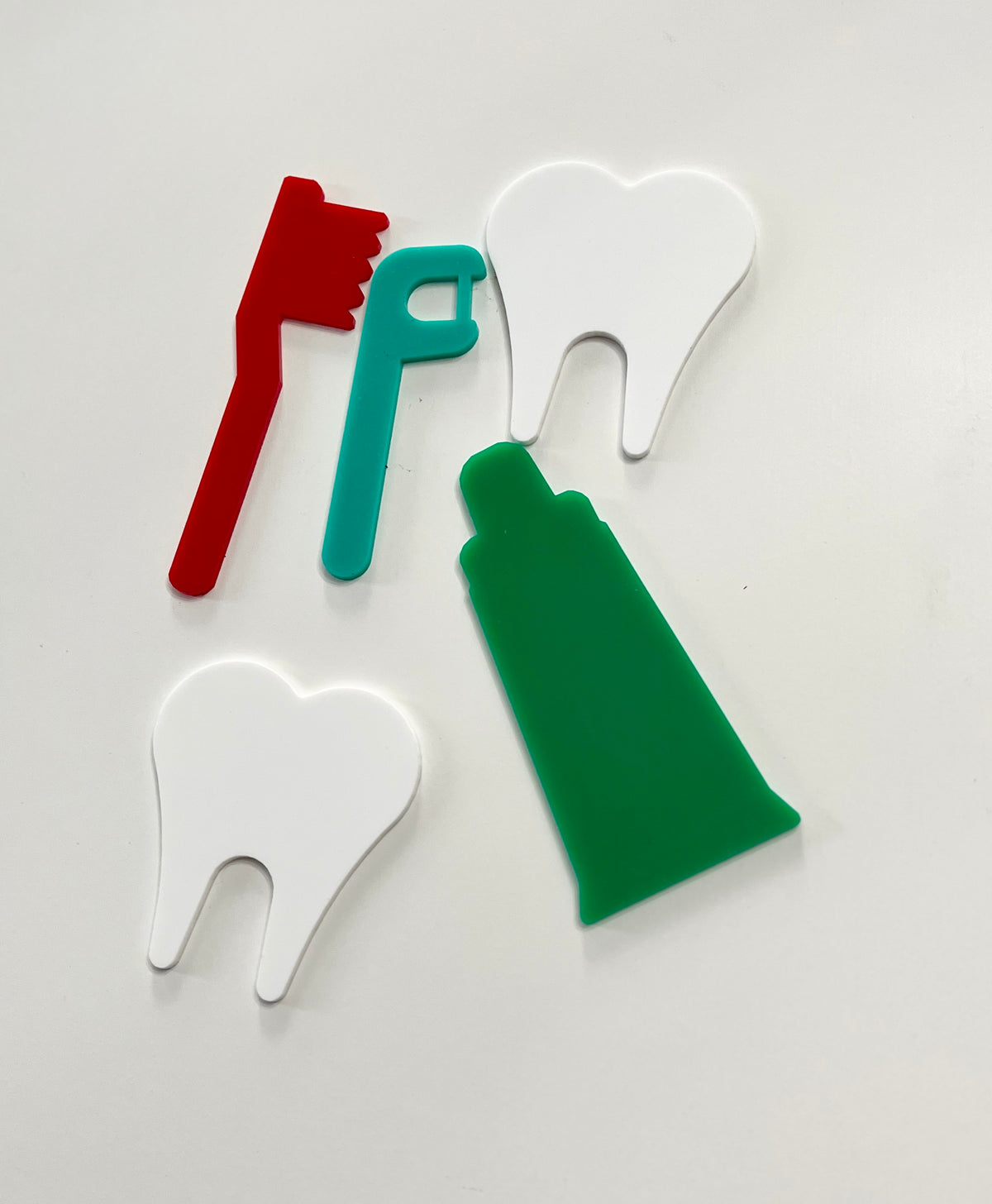 Set of colorful plastic dental care shapes including two teeth, a toothbrush, floss pick, and toothpaste tube on white background