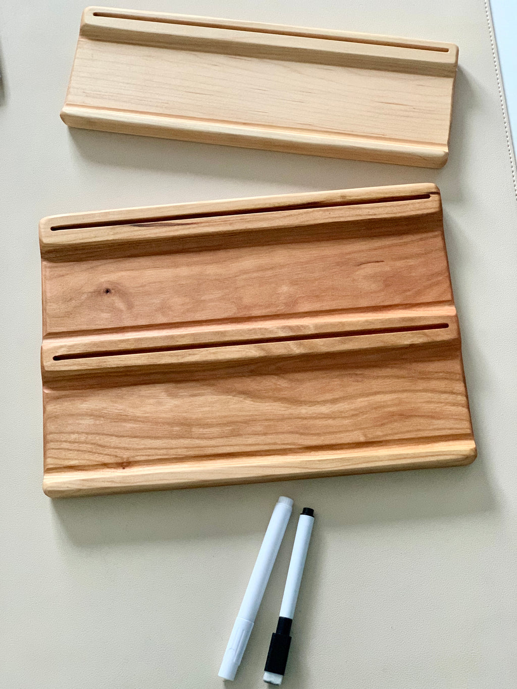 Two wooden boards with slots for holding markers accompanied by two dry erase markers on a light surface