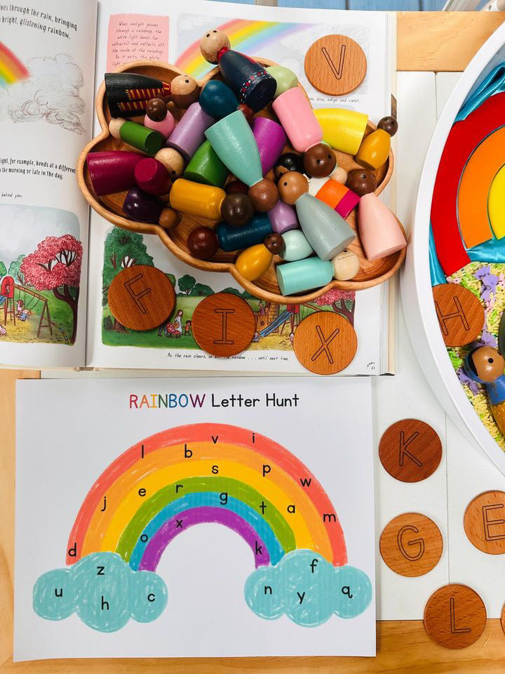 Wooden cloud-shaped sensory tray filled with colorful peg dolls surrounded by wooden letter discs and a rainbow letter hunt sheet