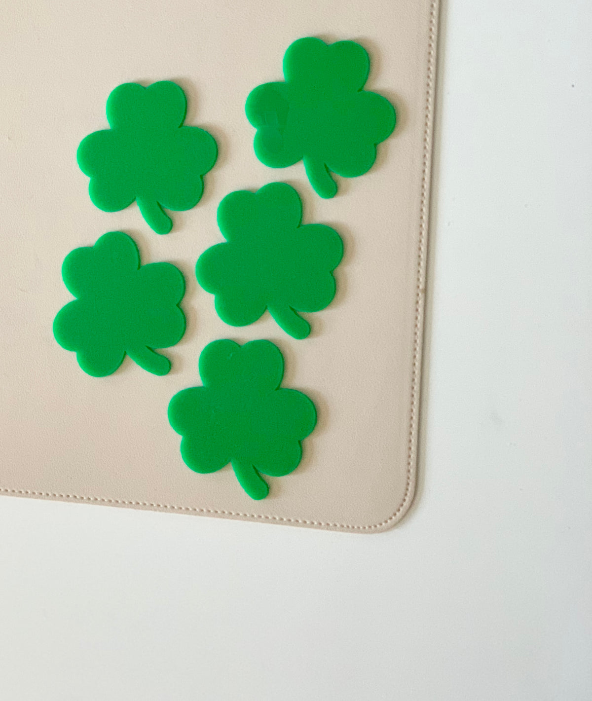Five bright green shamrock-shaped cutouts arranged on beige surface with stitched edges against white background
