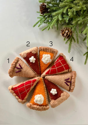 Eight colorful felt pie slice ornaments arranged in a circle with pine branches and cones nearby