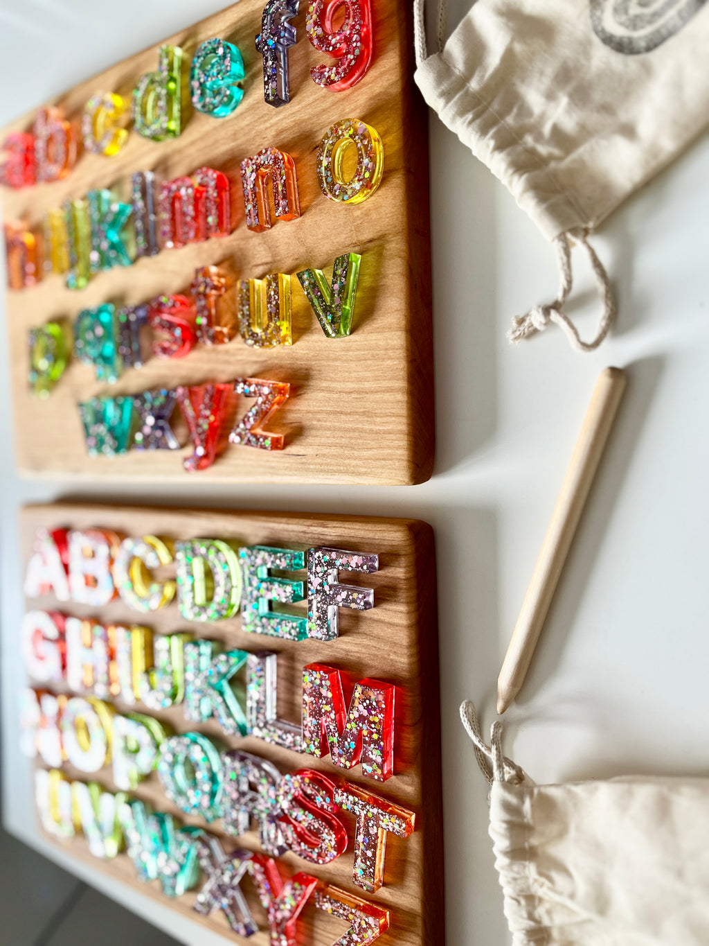 Two wooden alphabet boards with colorful resin uppercase and lowercase letters and a wooden stylus on white surface
