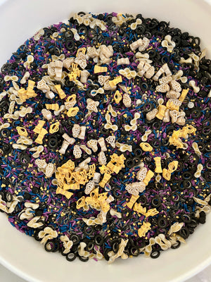 Mixed sensory rice dyed blue, purple, and black with yellow and white space-themed pasta shapes and black rings