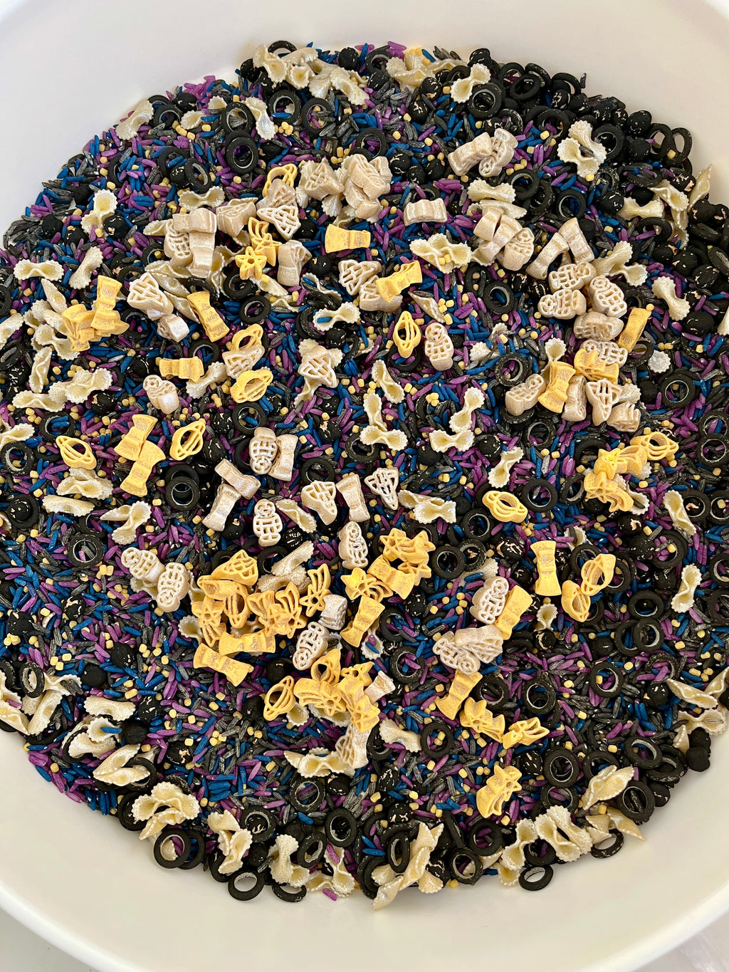Mixed sensory rice dyed blue, purple, and black with yellow and white space-themed pasta shapes and black rings