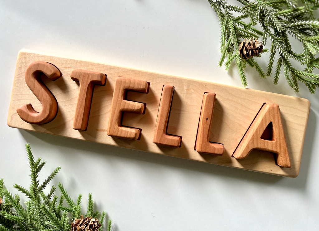 Personalized hardwood name puzzle spelling STELLA with uppercase letters on natural wood board with greenery accents