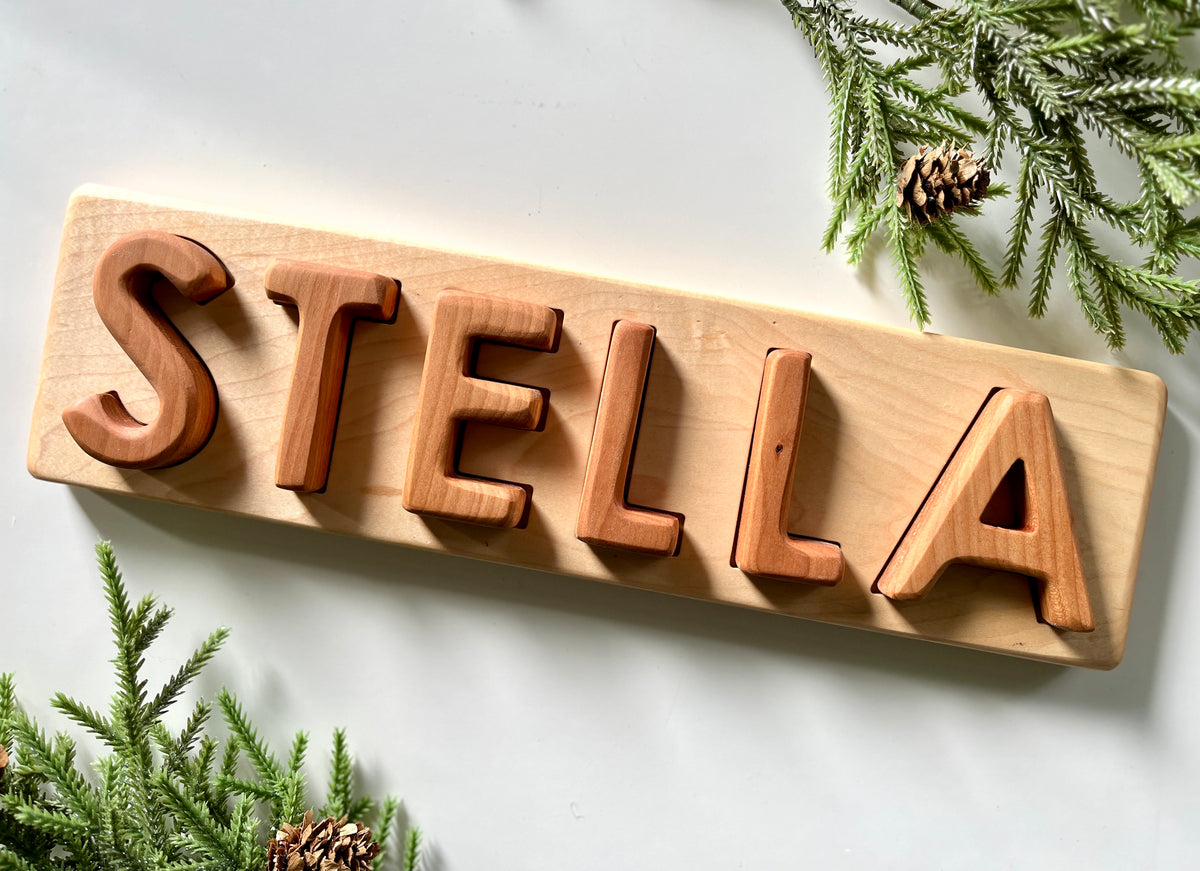 Personalized hardwood name puzzle spelling STELLA with uppercase letters on natural wood board with greenery accents