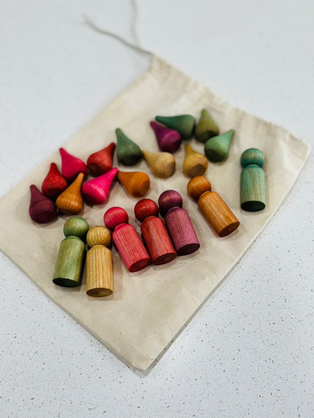 Collection of colorful wooden peg dolls and cone-shaped pieces arranged on a natural fabric drawstring bag