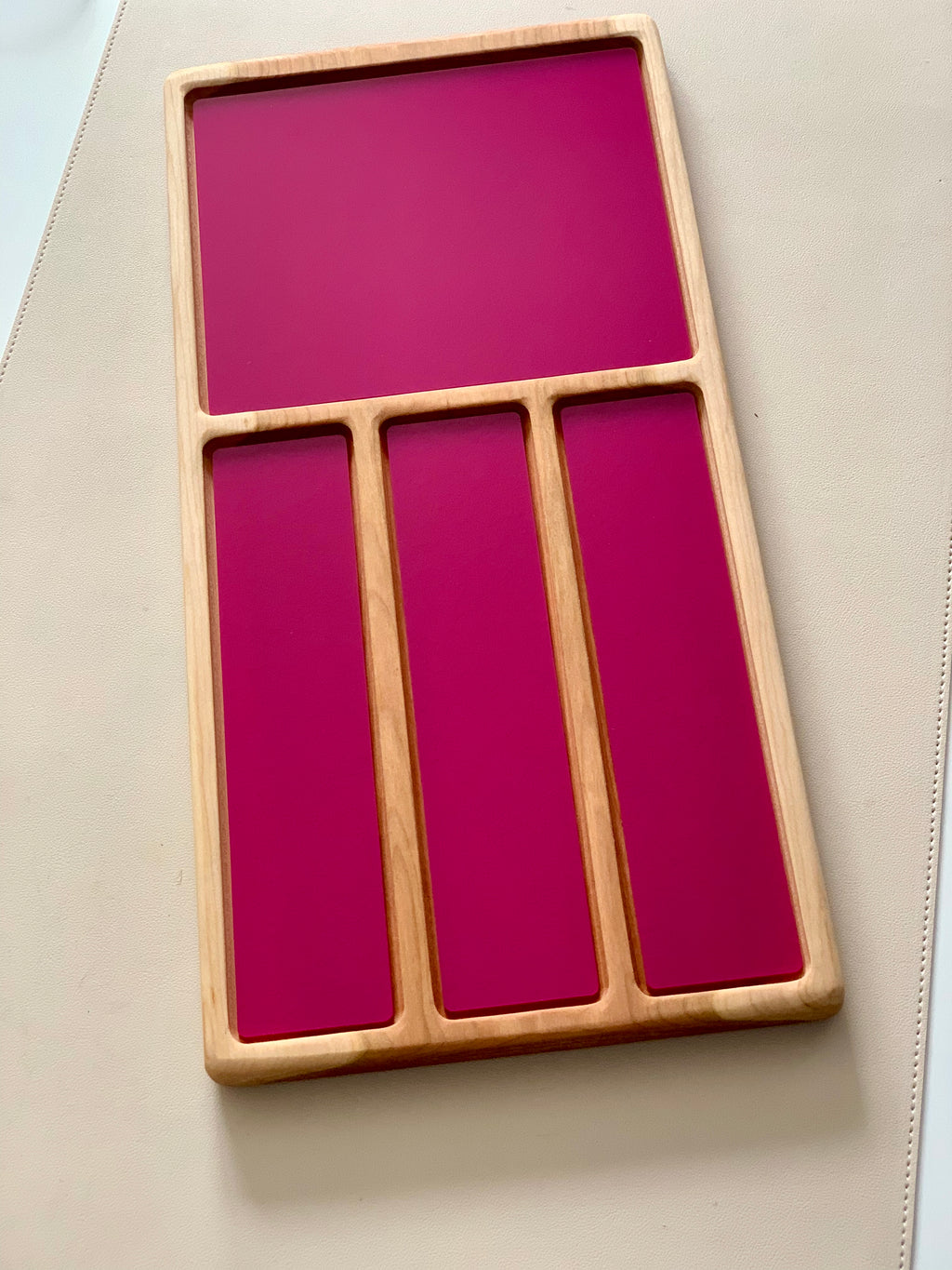 Wooden tray with one large rectangular and three narrow vertical compartments featuring deep pink panels on beige surface