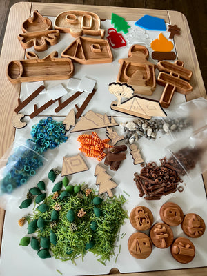 Wooden camping-themed trays and cutouts with trees, signs, campfire, tent, camper, colorful pasta, beads, and small natural elements on table