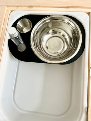 White tray with black silicone mat holding a large stainless steel bowl, small metal cup, and clear bottle on wooden surface